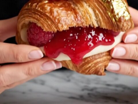 A close-up of a raspberry rose lychee supreme croissant, showing the layered pastry and pink cream filling.
