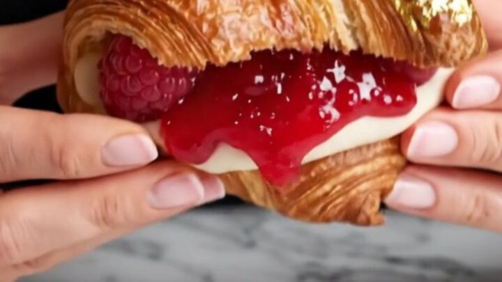 A close-up of a raspberry rose lychee supreme croissant, showing the layered pastry and pink cream filling.