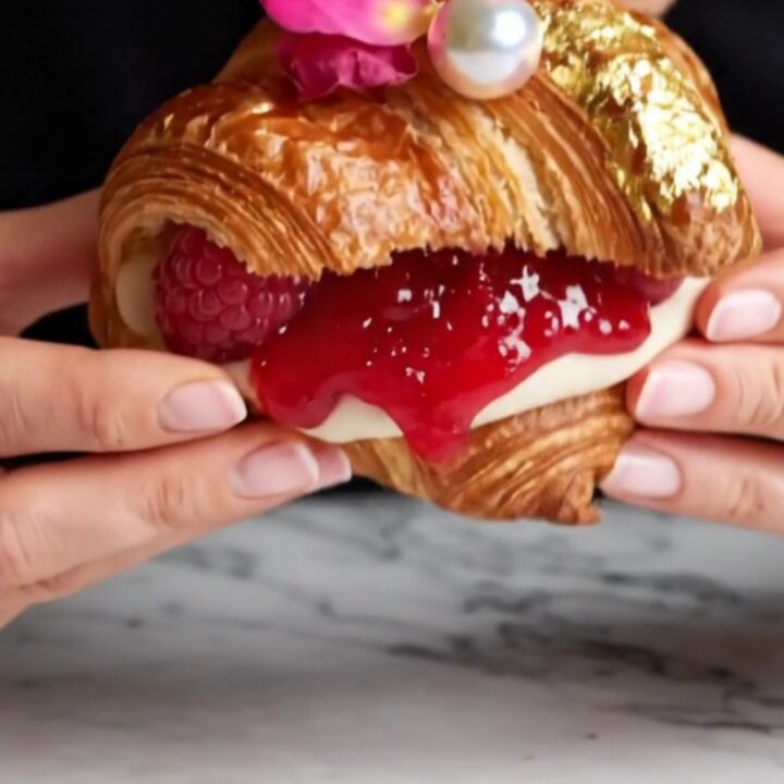 A close-up of a raspberry rose lychee supreme croissant, showing the layered pastry and pink cream filling.