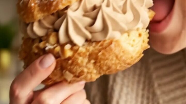 A close-up shot of a classic Paris-Brest pastry ring filled with rich hazelnut praline cream and topped with hazelnuts.