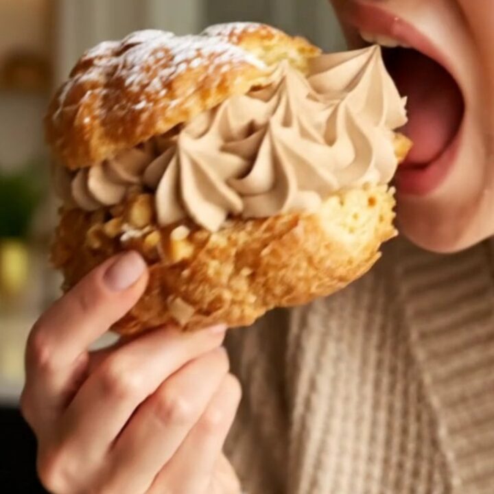A close-up shot of a classic Paris-Brest pastry ring filled with rich hazelnut praline cream and topped with hazelnuts.