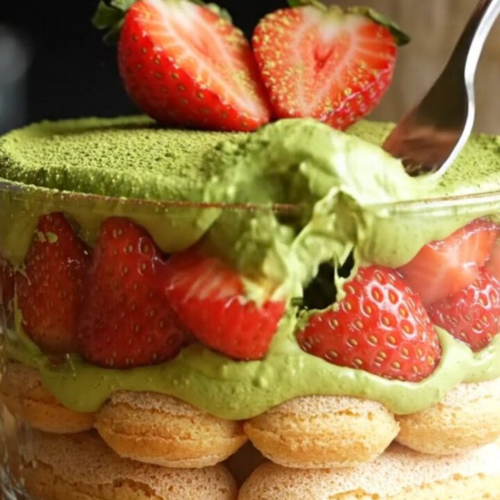 A vibrant Strawberry Matcha Tiramisu with green cream and red berries in a square glass dish.