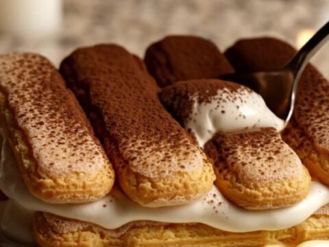A close-up of a creamy Italian tiramisu in a ceramic dish with a dusting of cocoa powder.