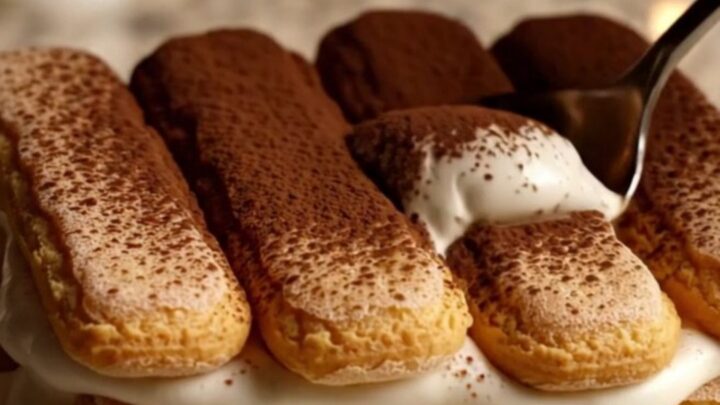 A close-up of a creamy Italian tiramisu in a ceramic dish with a dusting of cocoa powder.