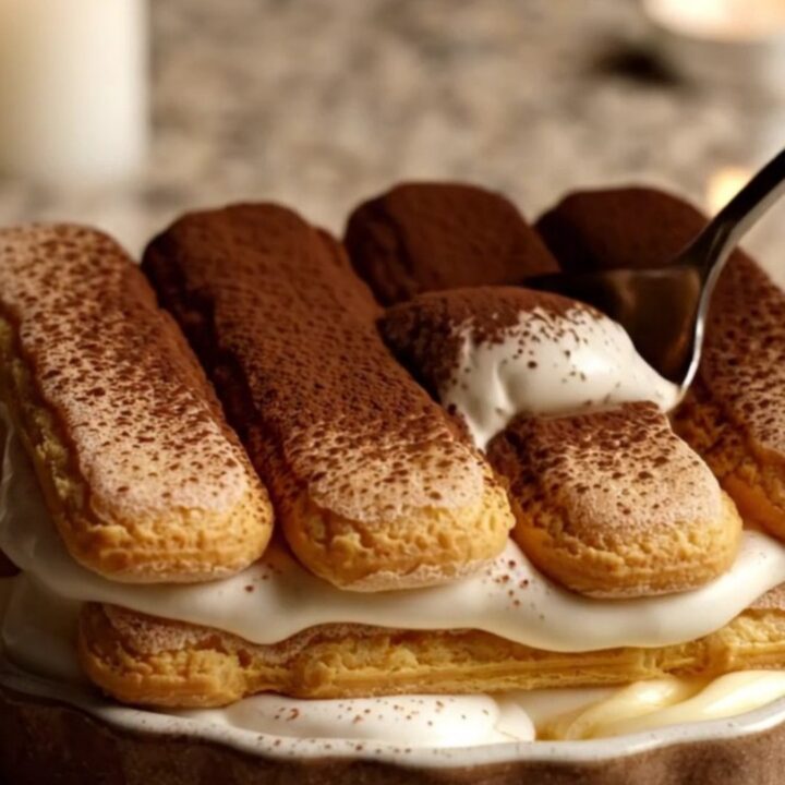 A close-up of a creamy Italian tiramisu in a ceramic dish with a dusting of cocoa powder.