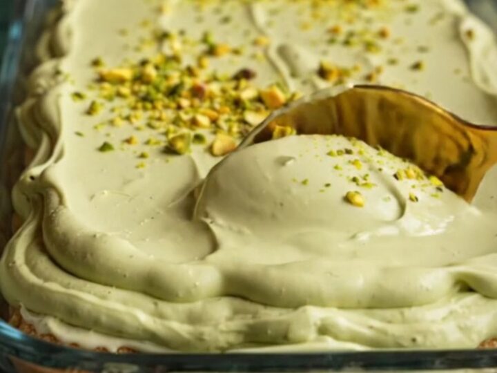 A close-up of a square of pistachio tiramisu showing distinct layers of green cream and soaked ladyfingers.
