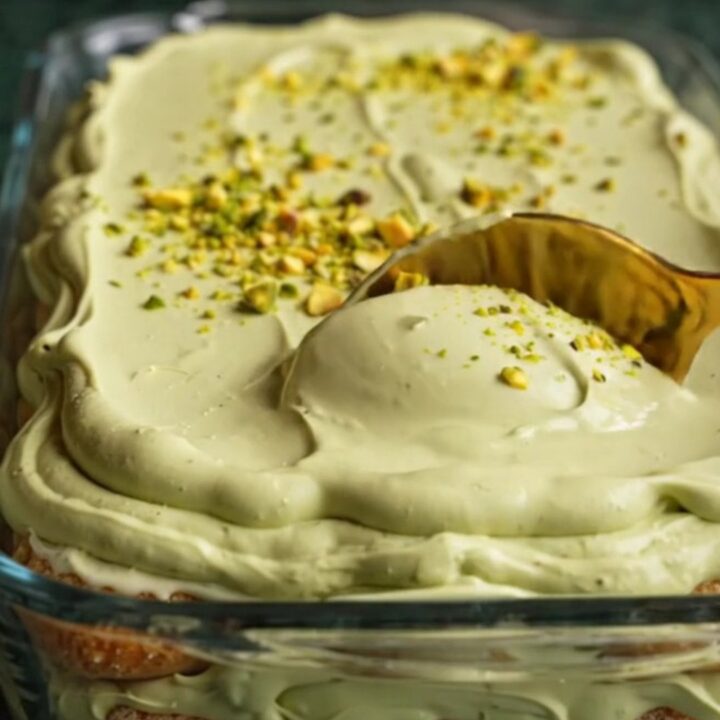A close-up of a square of pistachio tiramisu showing distinct layers of green cream and soaked ladyfingers.