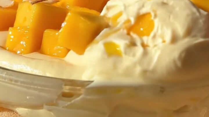 A close-up of a slice of creamy mango coconut tiramisu with fresh mango cubes, toasted coconut, and mint.