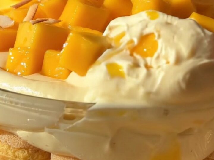 A close-up of a slice of creamy mango coconut tiramisu with fresh mango cubes, toasted coconut, and mint.