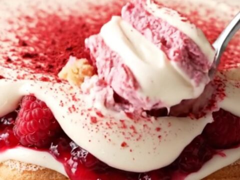 A close-up shot of a pink and ivory layered tiramisu in a glass dish, topped with bright freeze-dried raspberry powder.