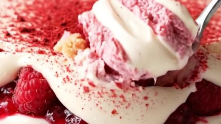 A close-up shot of a pink and ivory layered tiramisu in a glass dish, topped with bright freeze-dried raspberry powder.