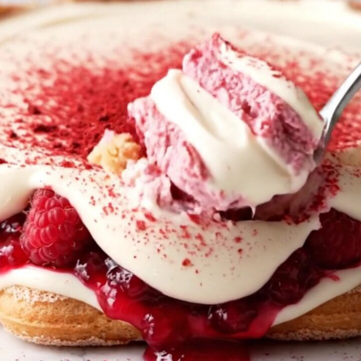 A close-up shot of a pink and ivory layered tiramisu in a glass dish, topped with bright freeze-dried raspberry powder.