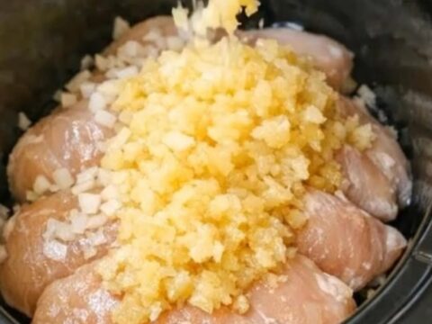 A close-up shot of tender shredded chicken coated in a glistening, sweet golden pineapple glaze in a slow cooker.