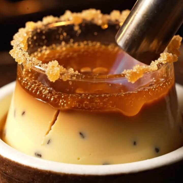 A close-up of a classic crème brûlée with a golden, shattered caramel crust in a rustic ceramic ramekin.