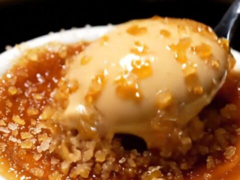 A close-up shot of a spoon cracking the dark, caramelized sugar crust of an espresso crème brûlée.