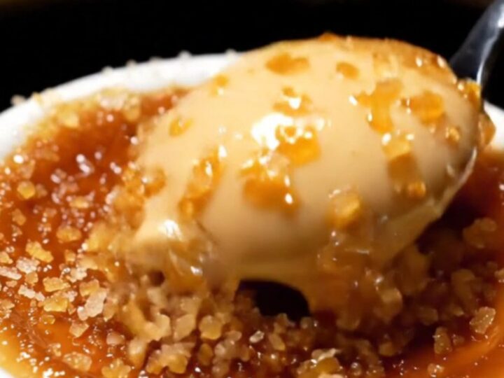 A close-up shot of a spoon cracking the dark, caramelized sugar crust of an espresso crème brûlée.
