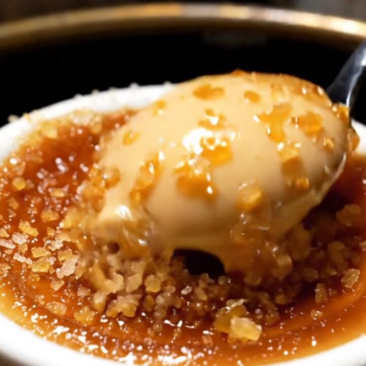 A close-up shot of a spoon cracking the dark, caramelized sugar crust of an espresso crème brûlée.