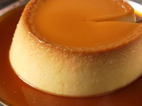 A golden French Crème Caramel flan unmolded on a white porcelain plate with a rich amber caramel sauce pooling around it.