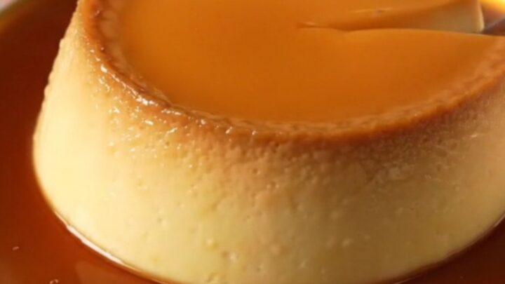 A golden French Crème Caramel flan unmolded on a white porcelain plate with a rich amber caramel sauce pooling around it.
