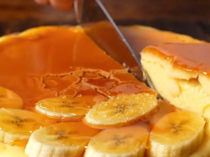 A close-up of a torched banana custard tart with a golden, crackling caramelized top and a crisp pastry crust.
