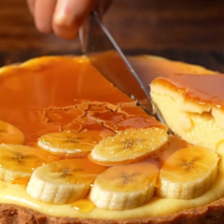 A close-up of a torched banana custard tart with a golden, crackling caramelized top and a crisp pastry crust.