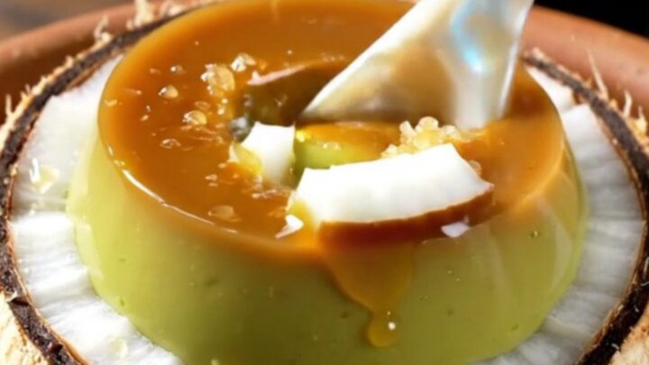 A close-up shot of a creamy green pandan crème brûlée inside a coconut shell with a caramelized sugar crust.
