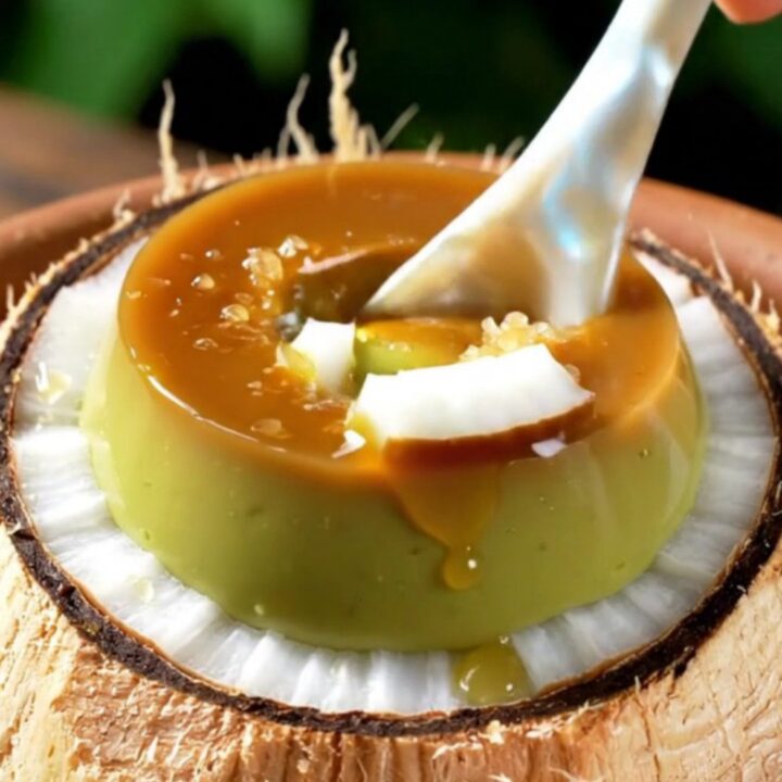 A close-up shot of a creamy green pandan crème brûlée inside a coconut shell with a caramelized sugar crust.