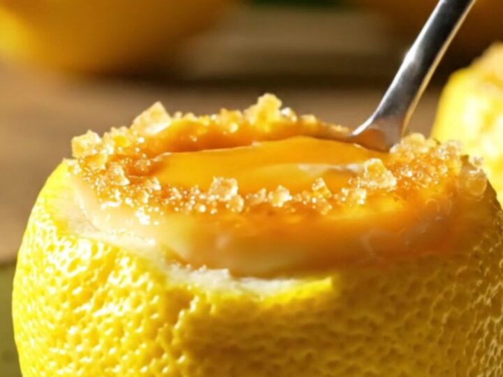 A close-up of a hollowed-out lemon shell filled with creamy lemon posset topped with a golden-brown torched sugar crust.