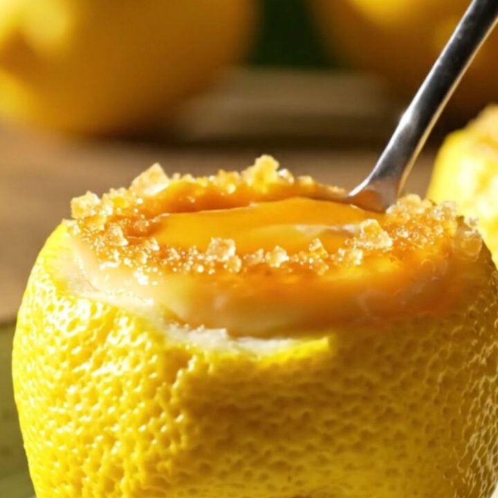 A close-up of a hollowed-out lemon shell filled with creamy lemon posset topped with a golden-brown torched sugar crust.