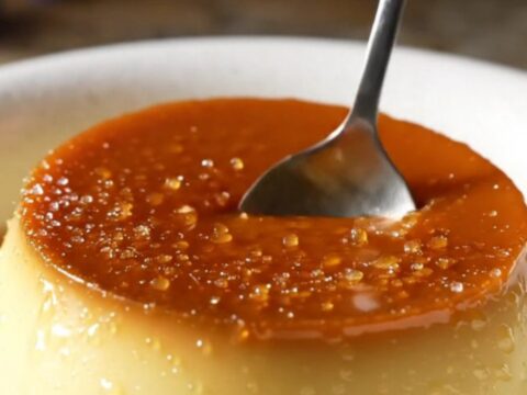 A close-up of a crème brûlée with a perfectly cracked golden caramel top and lavender garnish.