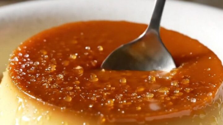 A close-up of a crème brûlée with a perfectly cracked golden caramel top and lavender garnish.