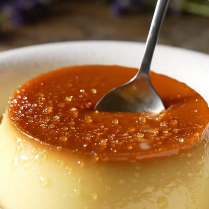 A close-up of a crème brûlée with a perfectly cracked golden caramel top and lavender garnish.