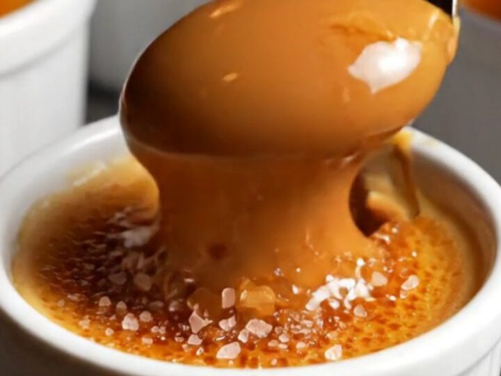 A close-up of a spoon cracking the golden-brown caramelized sugar shell of a dulce de leche crème brûlée.