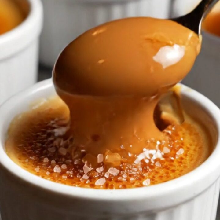 A close-up of a spoon cracking the golden-brown caramelized sugar shell of a dulce de leche crème brûlée.