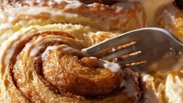 A close-up of a giant, pillowy cinnamon roll being pulled from a pan with frosting melting down the spirals.