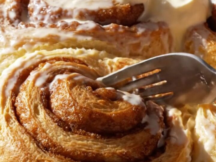 A close-up of a giant, pillowy cinnamon roll being pulled from a pan with frosting melting down the spirals.
