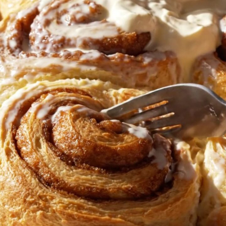 A close-up of a giant, pillowy cinnamon roll being pulled from a pan with frosting melting down the spirals.