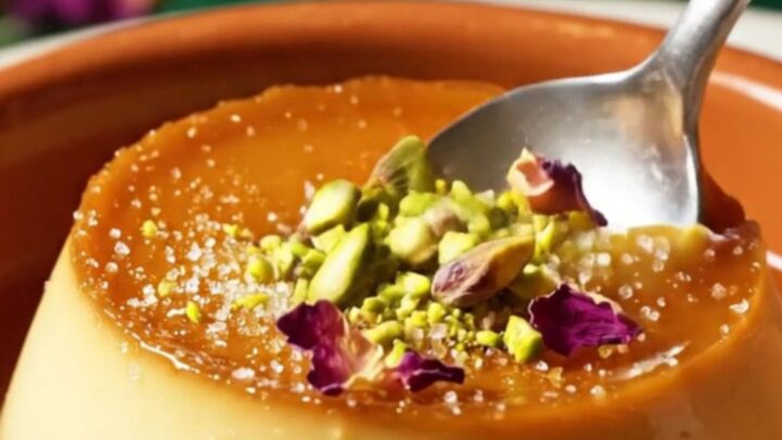 A close-up of a pistachio crème brûlée with a cracked caramel top and scattered emerald pistachios.