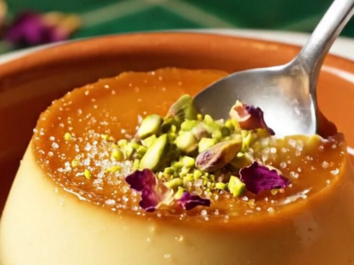 A close-up of a pistachio crème brûlée with a cracked caramel top and scattered emerald pistachios.