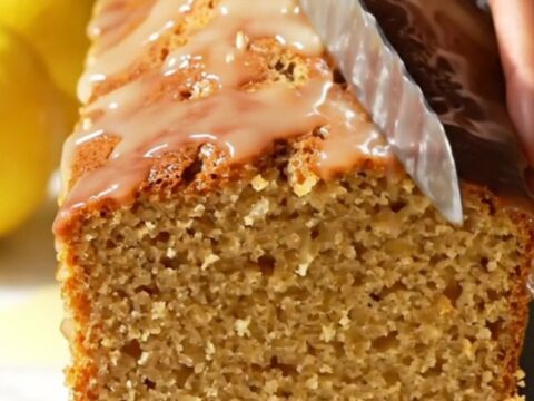 A slice of moist lemon loaf cake with a crisp, white crackle glaze on a marble surface.