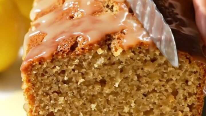 A slice of moist lemon loaf cake with a crisp, white crackle glaze on a marble surface.