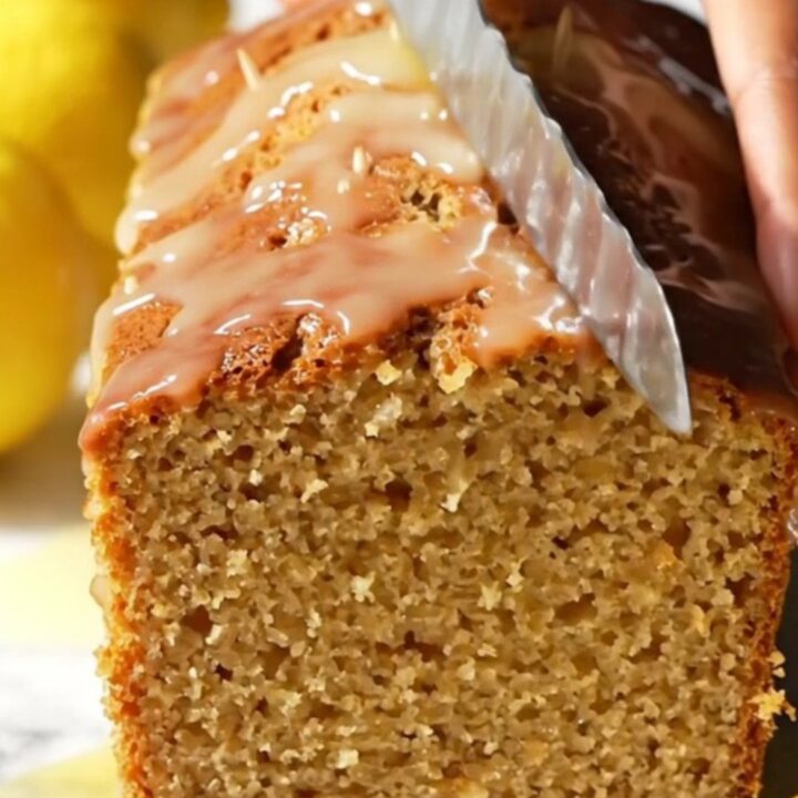 A slice of moist lemon loaf cake with a crisp, white crackle glaze on a marble surface.