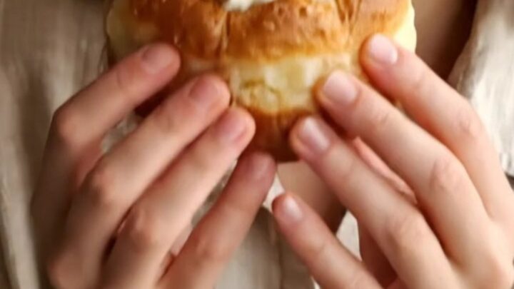 A close-up of a golden fried bomboloni being pulled apart, showing the creamy vanilla filling inside.