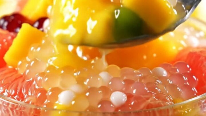 A clear bowl filled with creamy yellow mango sago topped with fresh mango cubes and ruby pomelo segments.