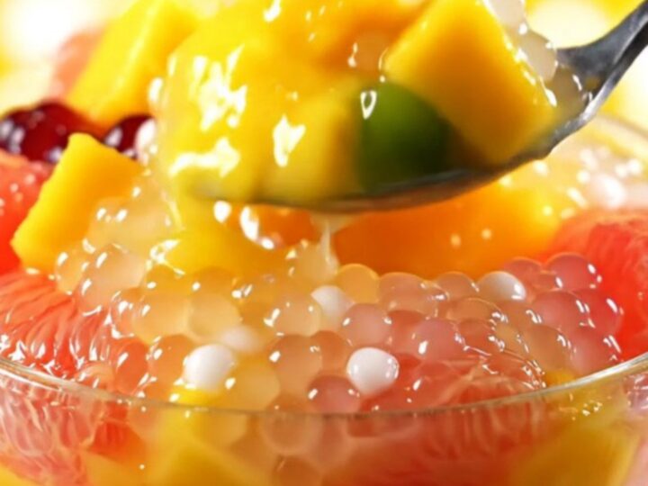 A clear bowl filled with creamy yellow mango sago topped with fresh mango cubes and ruby pomelo segments.