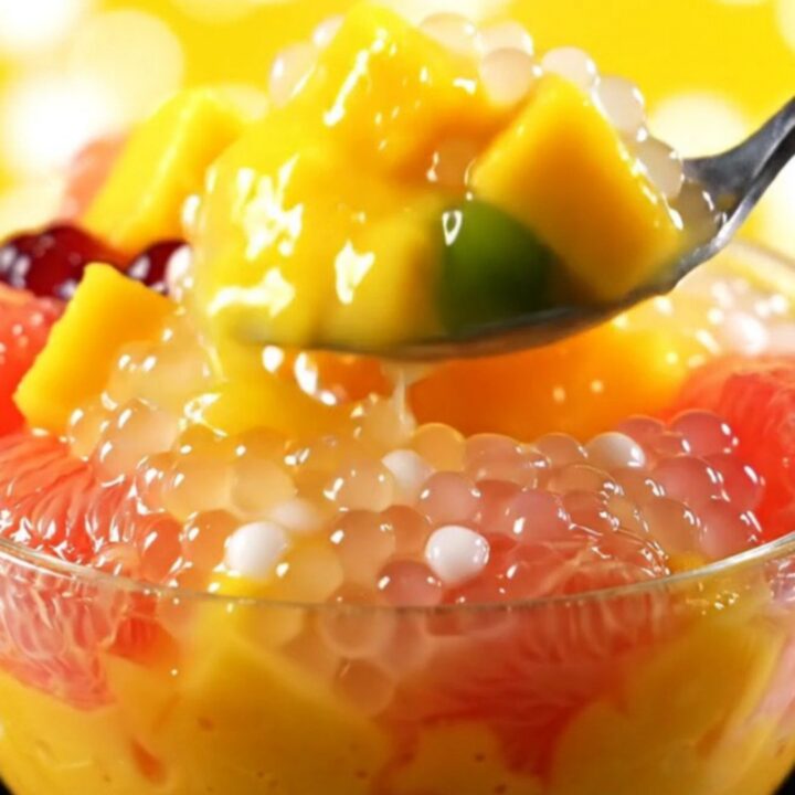 A clear bowl filled with creamy yellow mango sago topped with fresh mango cubes and ruby pomelo segments.