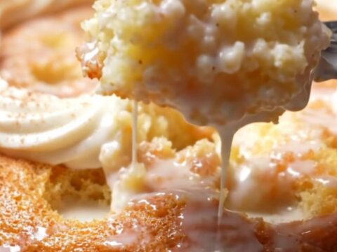A square of Tres Leches cake on a white plate with cream pooling around it.