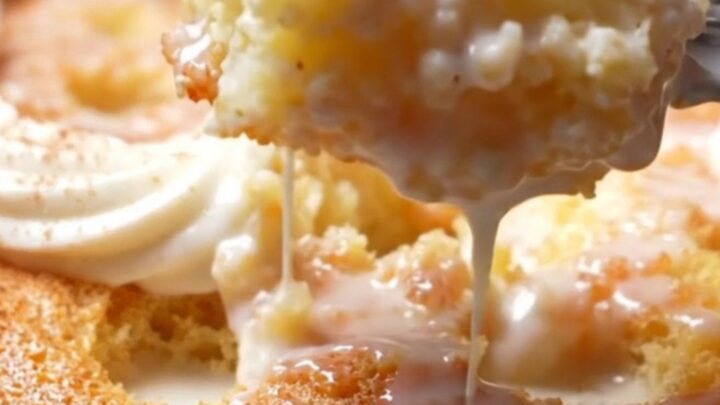 A square of Tres Leches cake on a white plate with cream pooling around it.