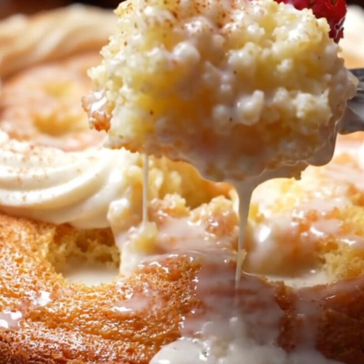 A square of Tres Leches cake on a white plate with cream pooling around it.