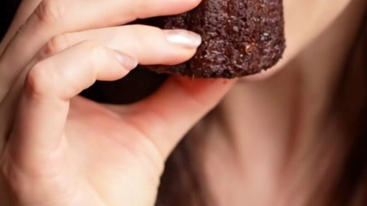 A close-up of a perfectly baked French Canelé with a dark, mahogany-colored, fluted exterior.